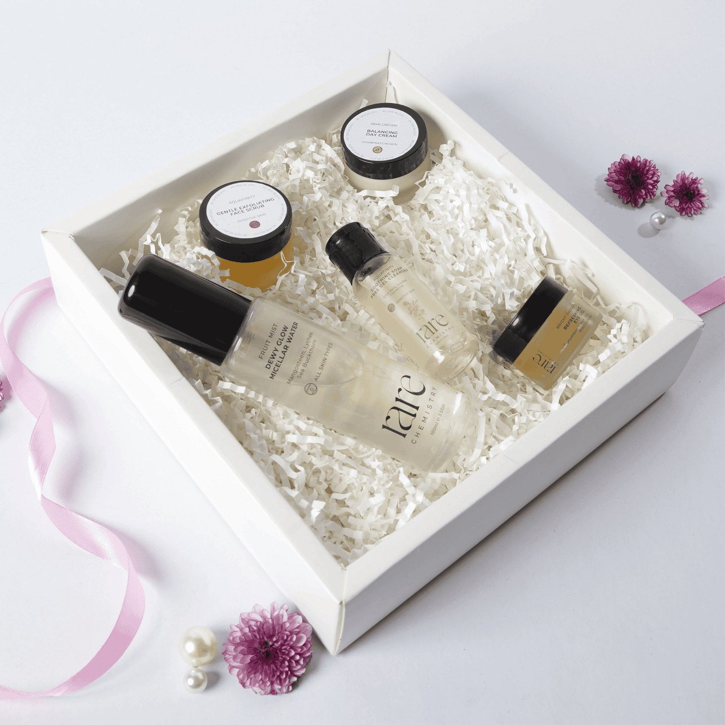 Set of skincare products in a white box with decorative flowers on a light background