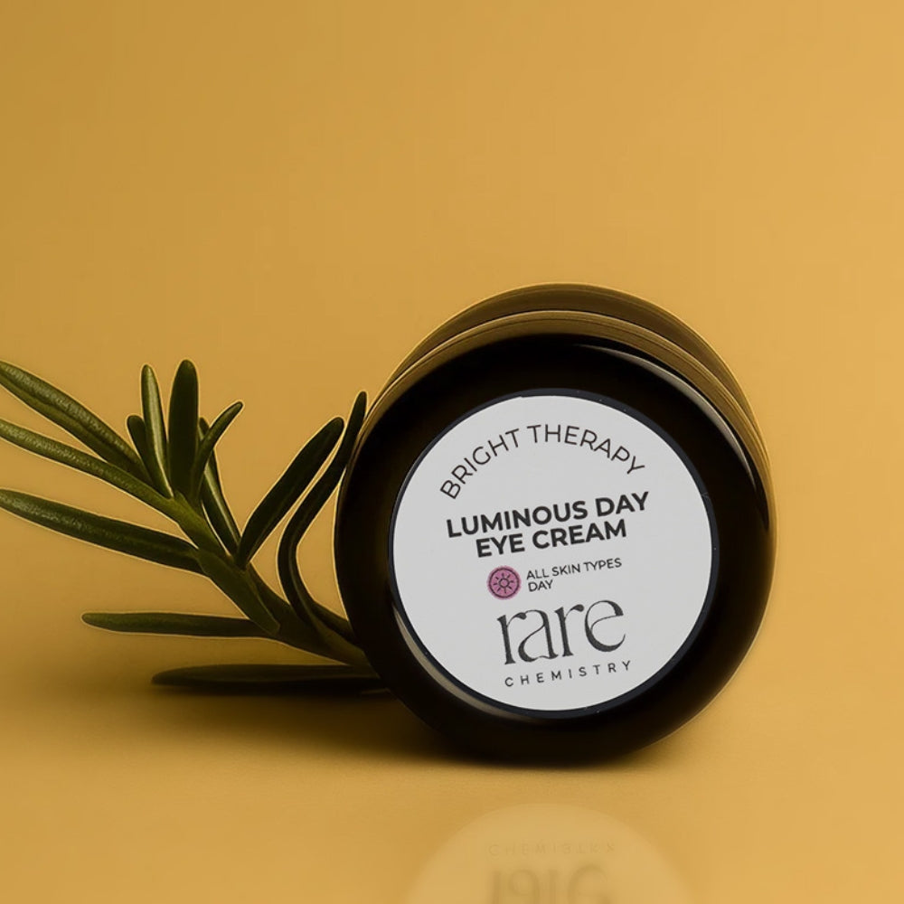 Jar of Luminous Day Eye Cream from rare chemistry on a yellow background with a green leaf.
