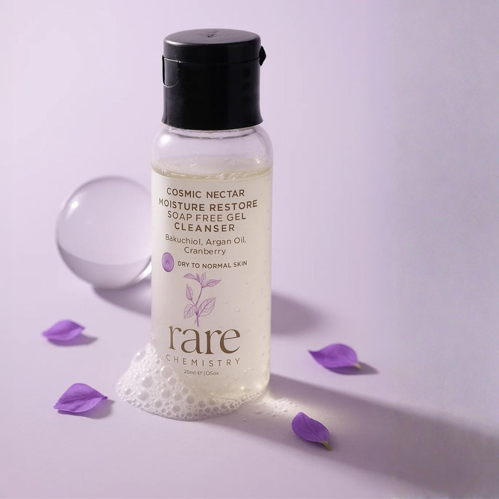 Bottle of 'Cosmic Nectar' moisture restore soap free gel cleanser by 'rare chemistry' on a light purple background with scattered purple flowers.